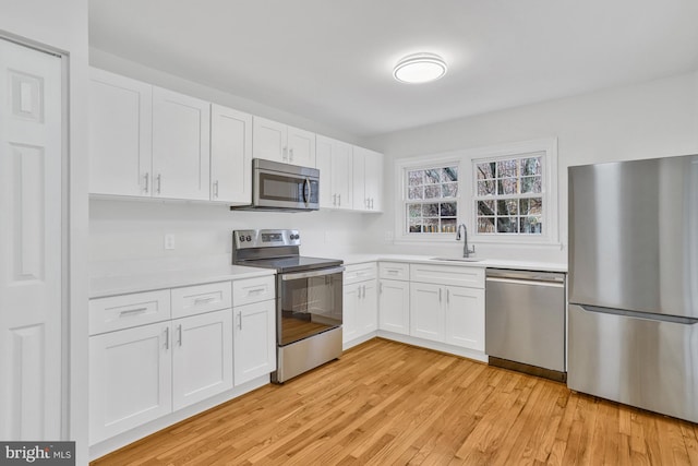 kitchen featuring stainless steel appliances, sink, white cabinets, and light hardwood / wood-style flooring