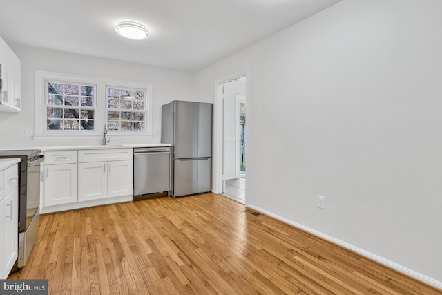 kitchen with stainless steel appliances, sink, white cabinets, and light hardwood / wood-style floors