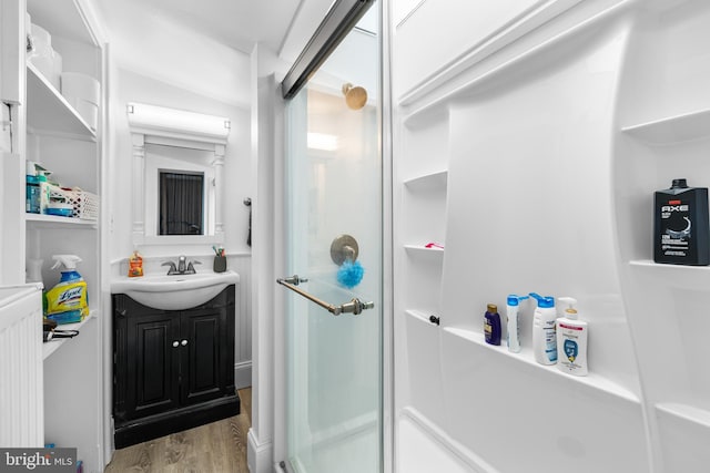 bathroom with vanity, hardwood / wood-style floors, a shower with shower door, and radiator heating unit