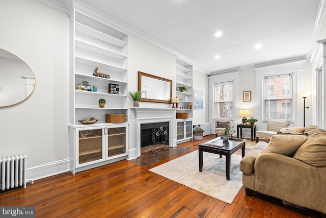 living room with crown molding, dark hardwood / wood-style floors, radiator, and built in features