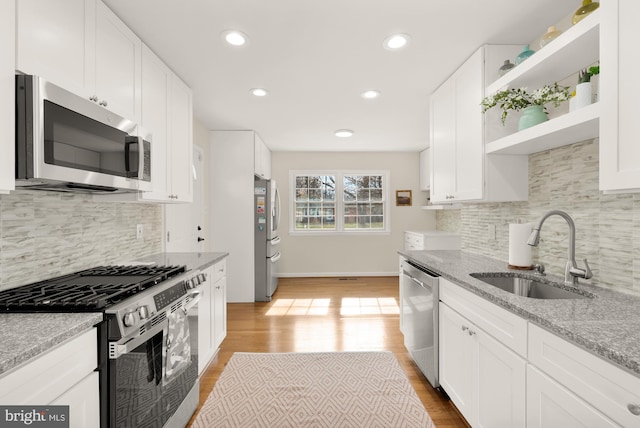 kitchen with white cabinetry, sink, light stone counters, stainless steel appliances, and light wood-type flooring