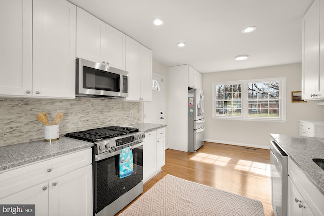 kitchen featuring tasteful backsplash, white cabinets, stainless steel appliances, light stone countertops, and light wood-type flooring