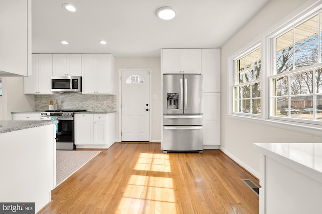 kitchen with backsplash, stainless steel appliances, light hardwood / wood-style floors, and white cabinets