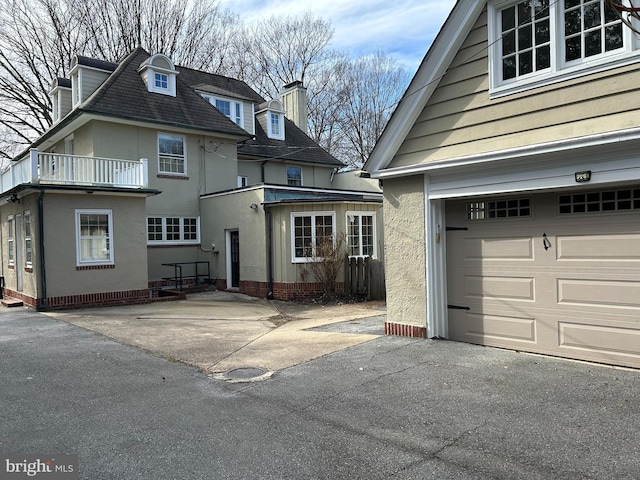 exterior space with aphalt driveway, stucco siding, a chimney, and a garage