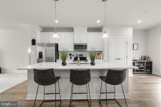 kitchen featuring appliances with stainless steel finishes, white cabinetry, an island with sink, sink, and light hardwood / wood-style floors