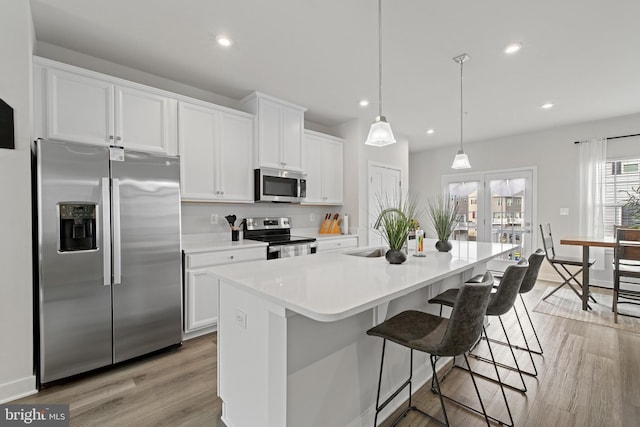 kitchen featuring white cabinetry, stainless steel appliances, a kitchen breakfast bar, a center island with sink, and decorative light fixtures