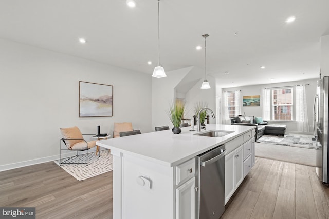 kitchen featuring decorative light fixtures, white cabinetry, an island with sink, sink, and stainless steel appliances