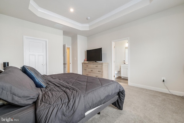 bedroom with ornamental molding, ensuite bathroom, a tray ceiling, and light carpet