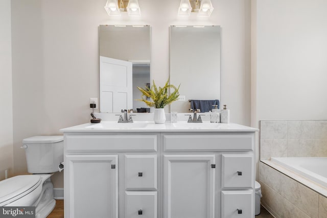 bathroom with vanity, toilet, and tiled bath