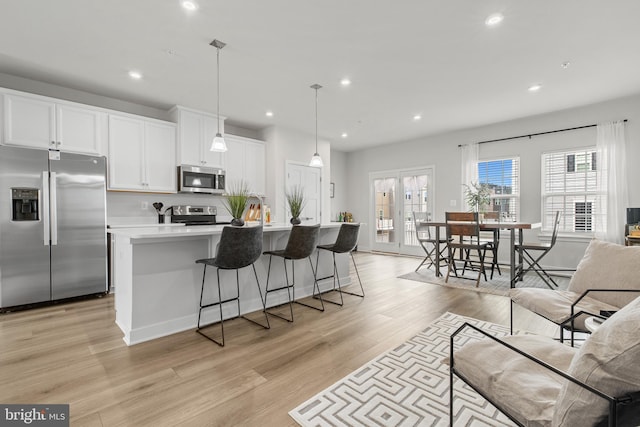 kitchen with a center island with sink, appliances with stainless steel finishes, pendant lighting, light hardwood / wood-style floors, and white cabinets