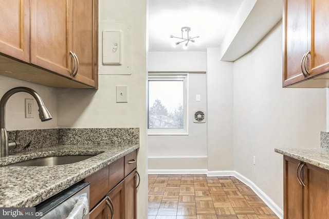 kitchen with light parquet floors, sink, stainless steel dishwasher, and light stone counters