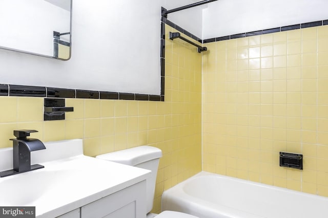 full bathroom with vanity, tiled shower / bath, tile walls, and toilet