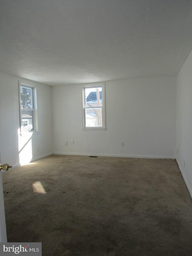 spare room featuring dark colored carpet and plenty of natural light