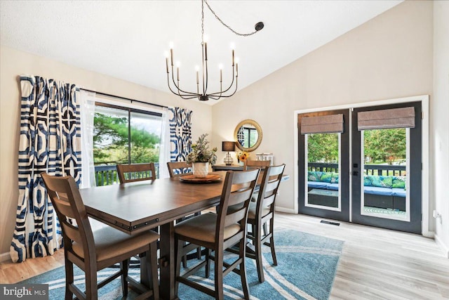 dining area featuring high vaulted ceiling, a chandelier, light hardwood / wood-style floors, and french doors