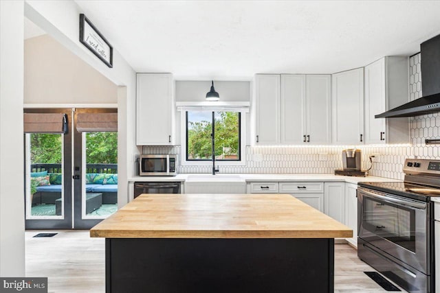 kitchen featuring stainless steel appliances, white cabinetry, a kitchen island, and wall chimney range hood