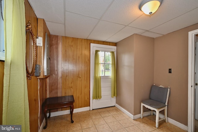 entryway featuring light tile patterned floors, a drop ceiling, and wood walls