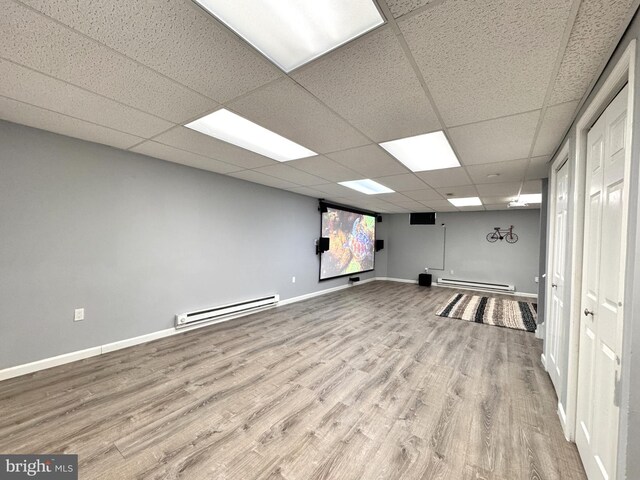 basement featuring a baseboard radiator, wood-type flooring, and a paneled ceiling