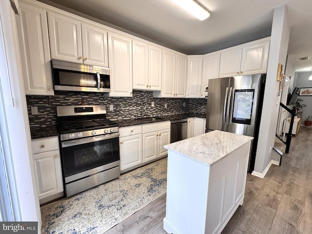 kitchen with appliances with stainless steel finishes, white cabinetry, backsplash, a center island, and light wood-type flooring