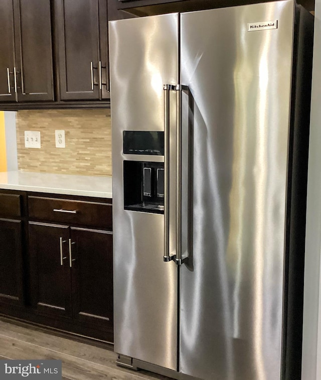 kitchen with tasteful backsplash, high quality fridge, wood finished floors, light countertops, and dark brown cabinets