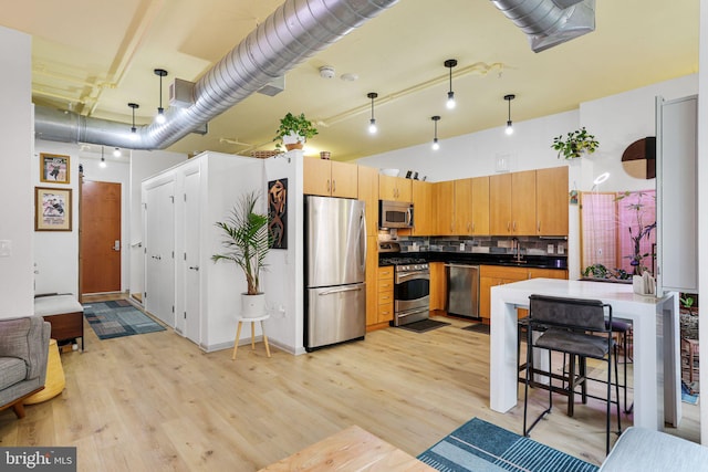 kitchen with stainless steel appliances, decorative light fixtures, sink, and light wood-type flooring