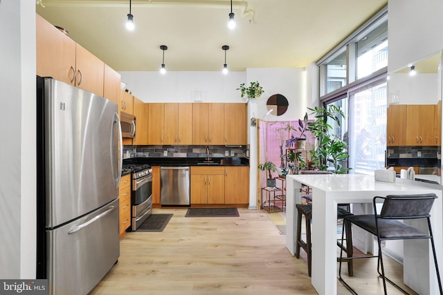 kitchen featuring sink, decorative light fixtures, light hardwood / wood-style flooring, stainless steel appliances, and decorative backsplash