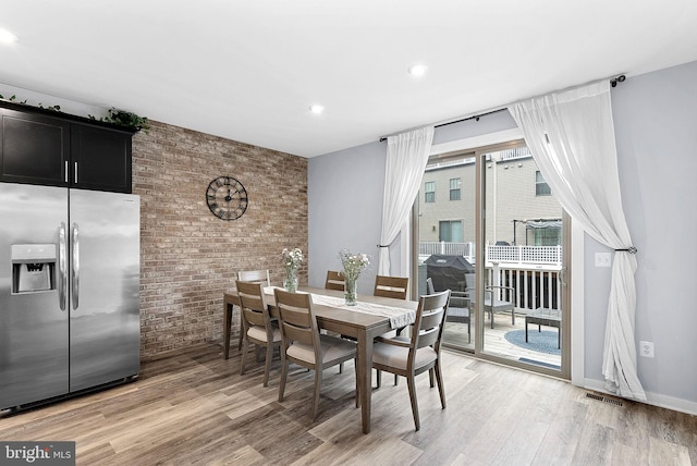 dining room with baseboards, brick wall, visible vents, and wood finished floors