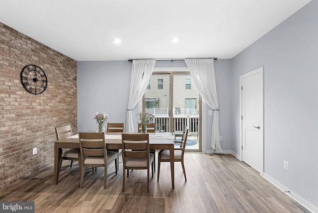 dining space with brick wall, wood finished floors, and baseboards