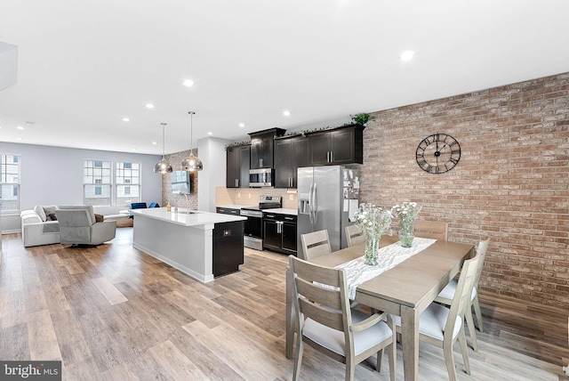 kitchen with appliances with stainless steel finishes, open floor plan, a kitchen island with sink, light countertops, and pendant lighting