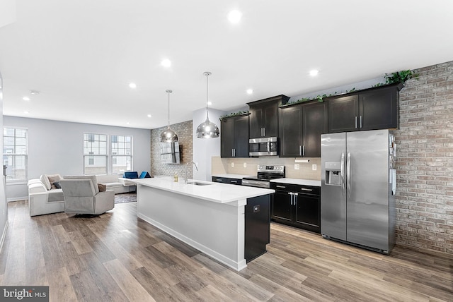 kitchen with appliances with stainless steel finishes, open floor plan, decorative light fixtures, a kitchen island with sink, and a sink