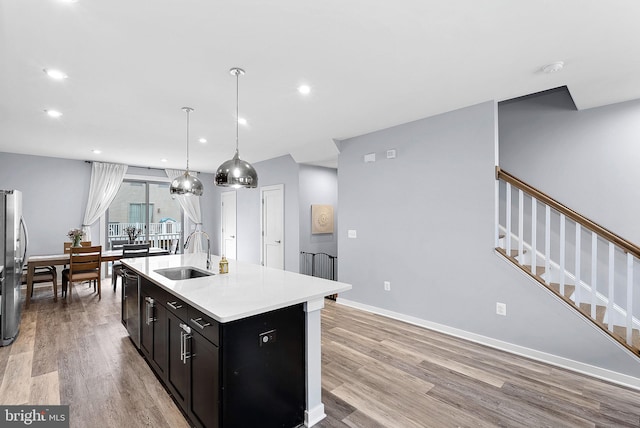 kitchen with a kitchen island with sink, a sink, light countertops, light wood-type flooring, and freestanding refrigerator