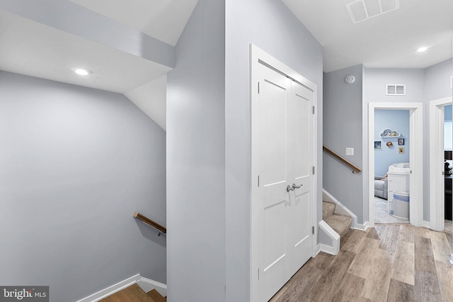 hall with light wood-style floors, visible vents, baseboards, and stairs