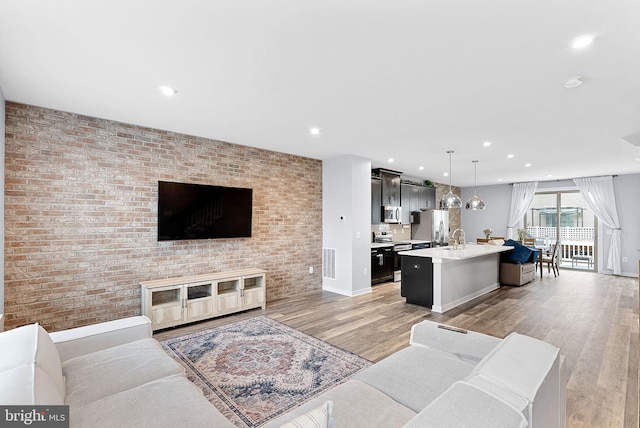 living area featuring recessed lighting, visible vents, light wood-style flooring, and brick wall