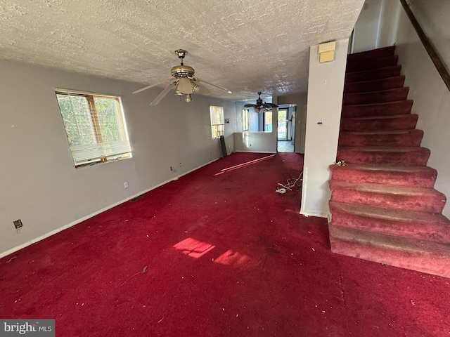 unfurnished living room with ceiling fan, carpet flooring, a textured ceiling, and a wealth of natural light