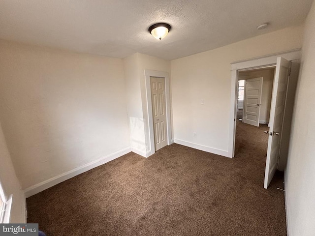 unfurnished bedroom featuring baseboards, a closet, dark carpet, and a textured ceiling