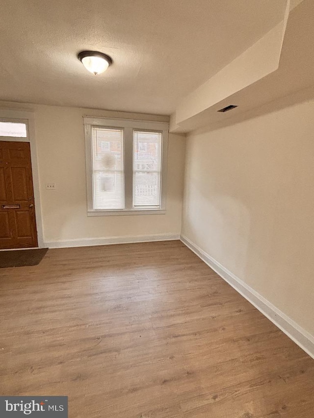 unfurnished room featuring a textured ceiling, wood finished floors, visible vents, and baseboards