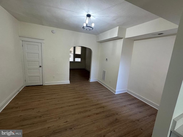 unfurnished dining area with arched walkways, dark wood-style floors, visible vents, and baseboards