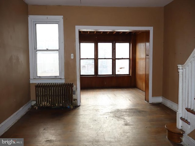 empty room with a healthy amount of sunlight, radiator heating unit, and hardwood / wood-style floors