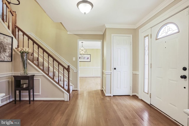 foyer with stairway, hardwood / wood-style flooring, crown molding, a decorative wall, and a notable chandelier