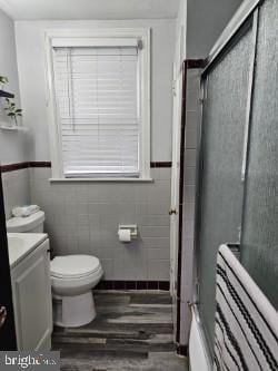 bathroom featuring walk in shower, toilet, tile walls, vanity, and hardwood / wood-style floors