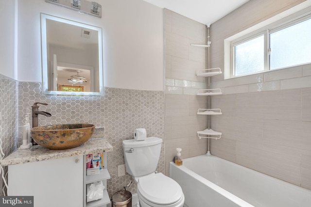 bathroom featuring tile walls, vanity, a tub, and toilet