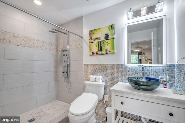 bathroom with tiled shower, vanity, toilet, and tile walls