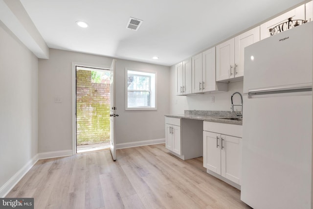 kitchen with sink, white cabinetry, white refrigerator, light stone countertops, and light hardwood / wood-style floors