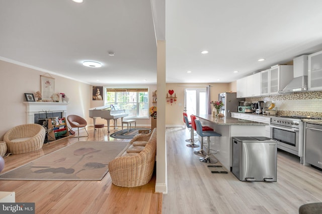 kitchen featuring white cabinetry, a kitchen breakfast bar, decorative backsplash, stainless steel appliances, and wall chimney exhaust hood