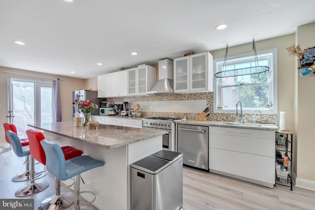 kitchen with a kitchen island, sink, white cabinets, stainless steel appliances, and wall chimney exhaust hood