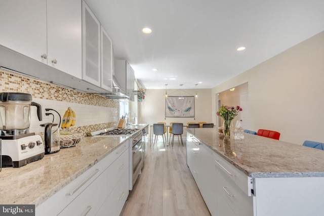 kitchen featuring light wood-type flooring, white cabinets, a kitchen bar, and high end stove