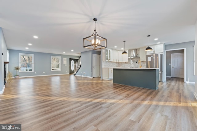 kitchen with wall chimney exhaust hood, white cabinetry, decorative light fixtures, a center island, and stainless steel refrigerator