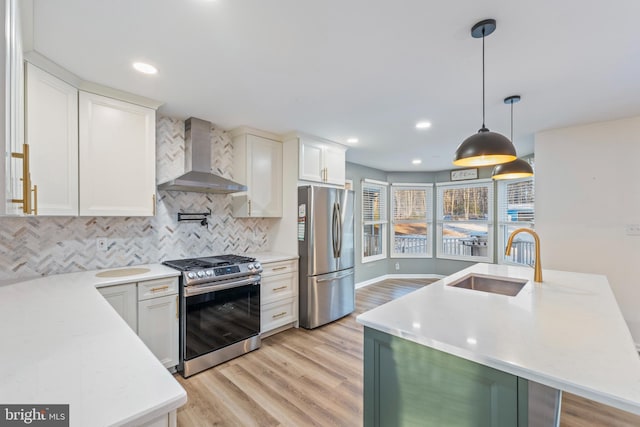 kitchen featuring wall chimney range hood, sink, appliances with stainless steel finishes, white cabinetry, and hanging light fixtures