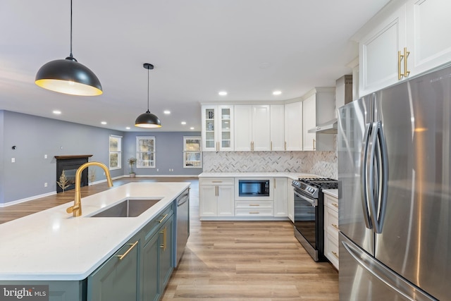 kitchen with pendant lighting, sink, appliances with stainless steel finishes, white cabinets, and wall chimney exhaust hood