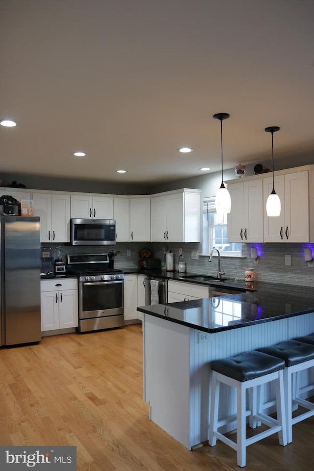 kitchen featuring sink, white cabinetry, hanging light fixtures, a kitchen breakfast bar, and stainless steel appliances