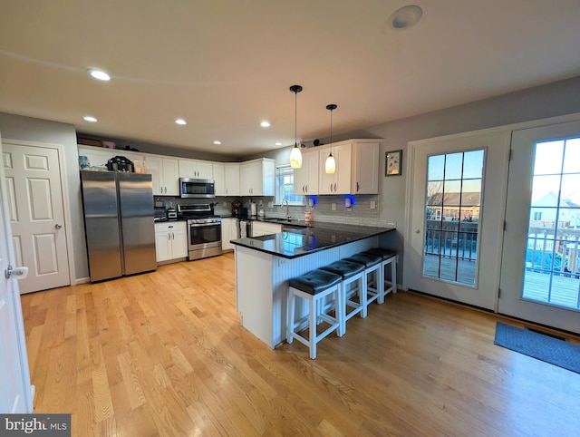 kitchen featuring sink, white cabinetry, decorative light fixtures, appliances with stainless steel finishes, and kitchen peninsula